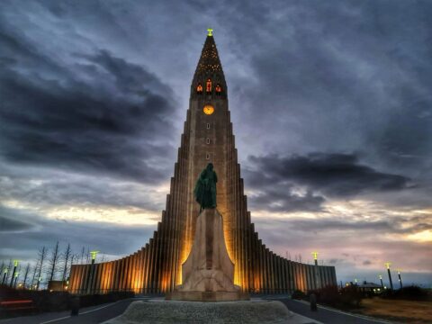 Upplyst kyrkobyggnad med staty framför under en dramatisk kvällshimmel